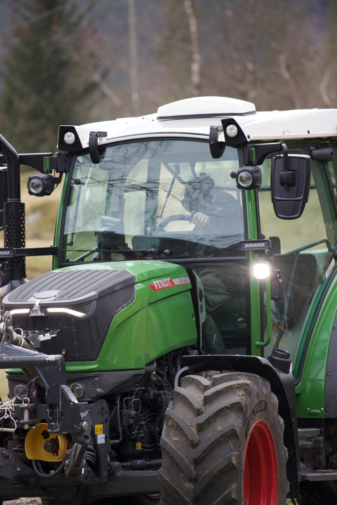 A green tractor operated by a person in rural setting, showcasing modern agriculture.